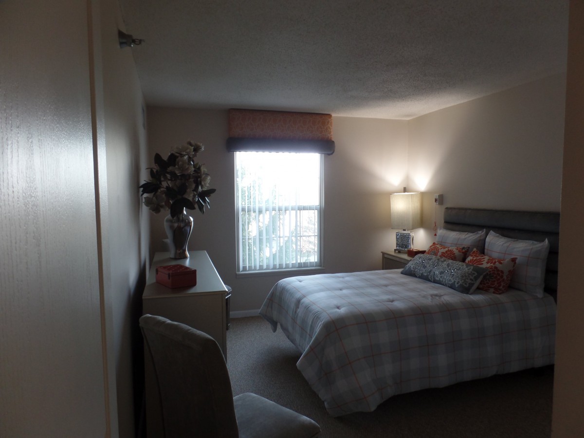 A cozy bedroom with a neatly made bed, side table lamp, and window with curtains.