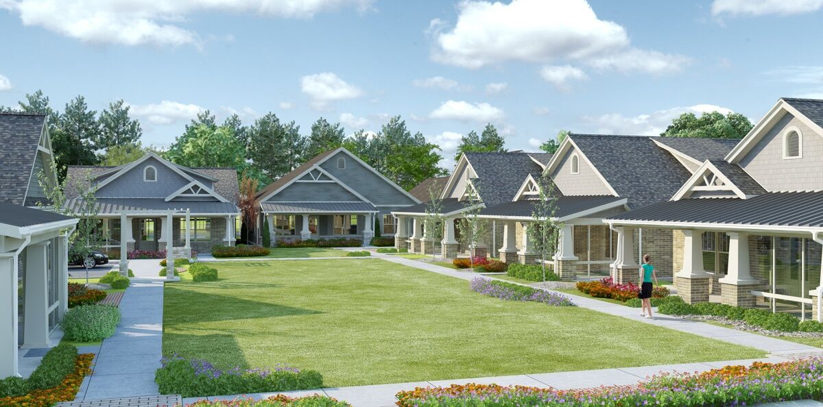 A view of a residential area with multiple houses, well-maintained lawns, and surrounding trees under a clear sky.