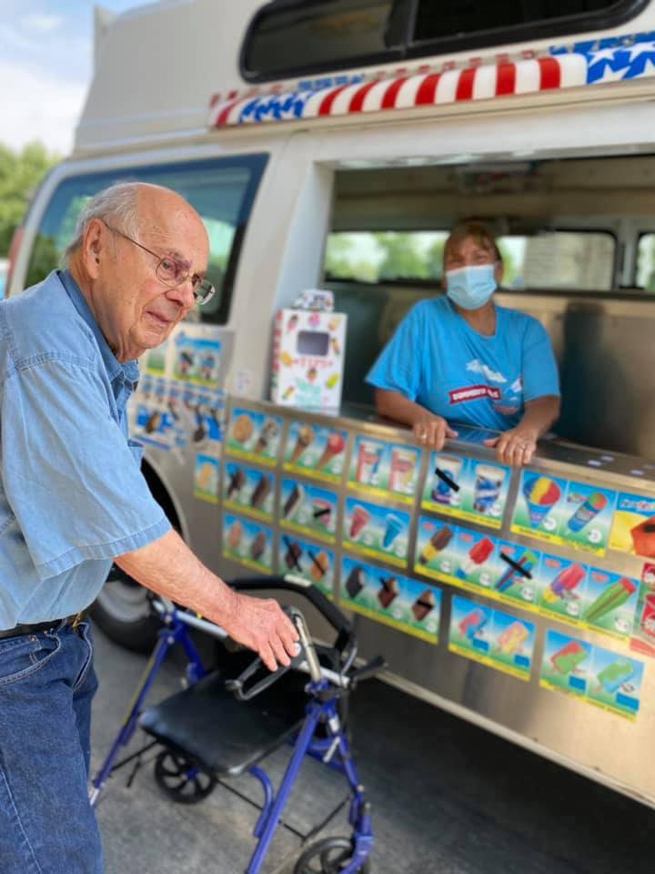 A senior man with a walker buying ice cream from a vendor at an ice cream truck.