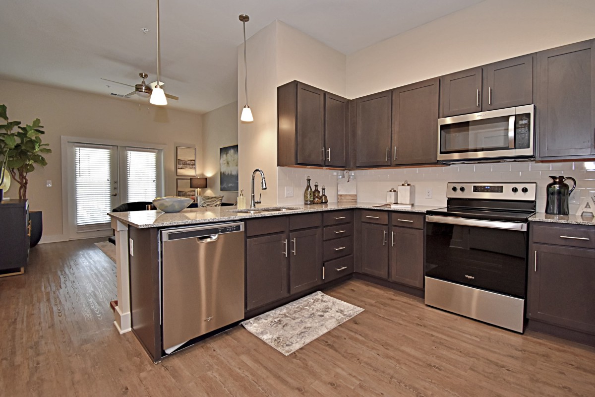 A modern kitchen featuring stainless steel appliances and wooden cabinets, with an open plan design that emphasizes natural light.