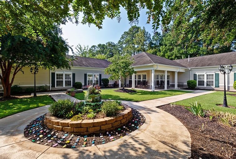 A scenic view of a landscaped garden with a circular flower bed and pathways surrounding a residential building.