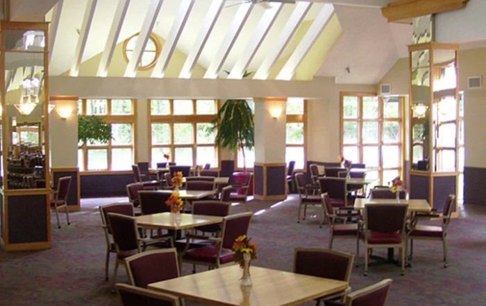 A spacious dining area with tables and chairs, illuminated by natural sunlight through large windows.