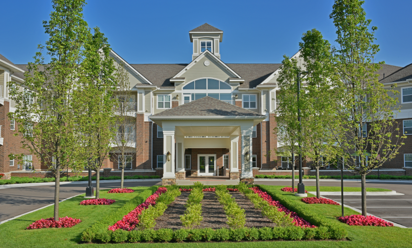 A beautifully landscaped building entrance with a symmetrical pathway and vibrant flower beds on a sunny day.