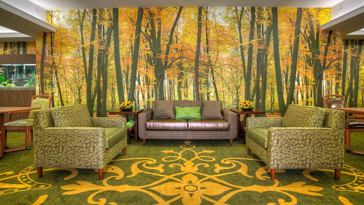 A cozy living room featuring a forest-themed mural with autumn colors, complemented by comfortable seating and a nature-inspired carpet design.