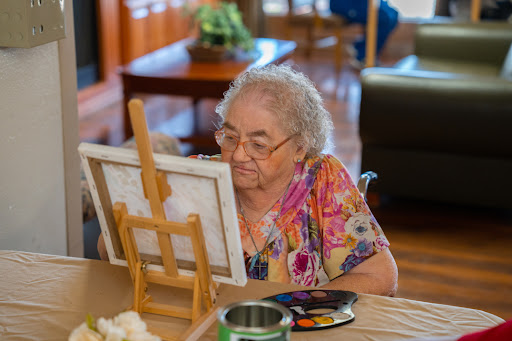 An elderly woman enjoying her time painting at an easel in a cozy indoor setting.
