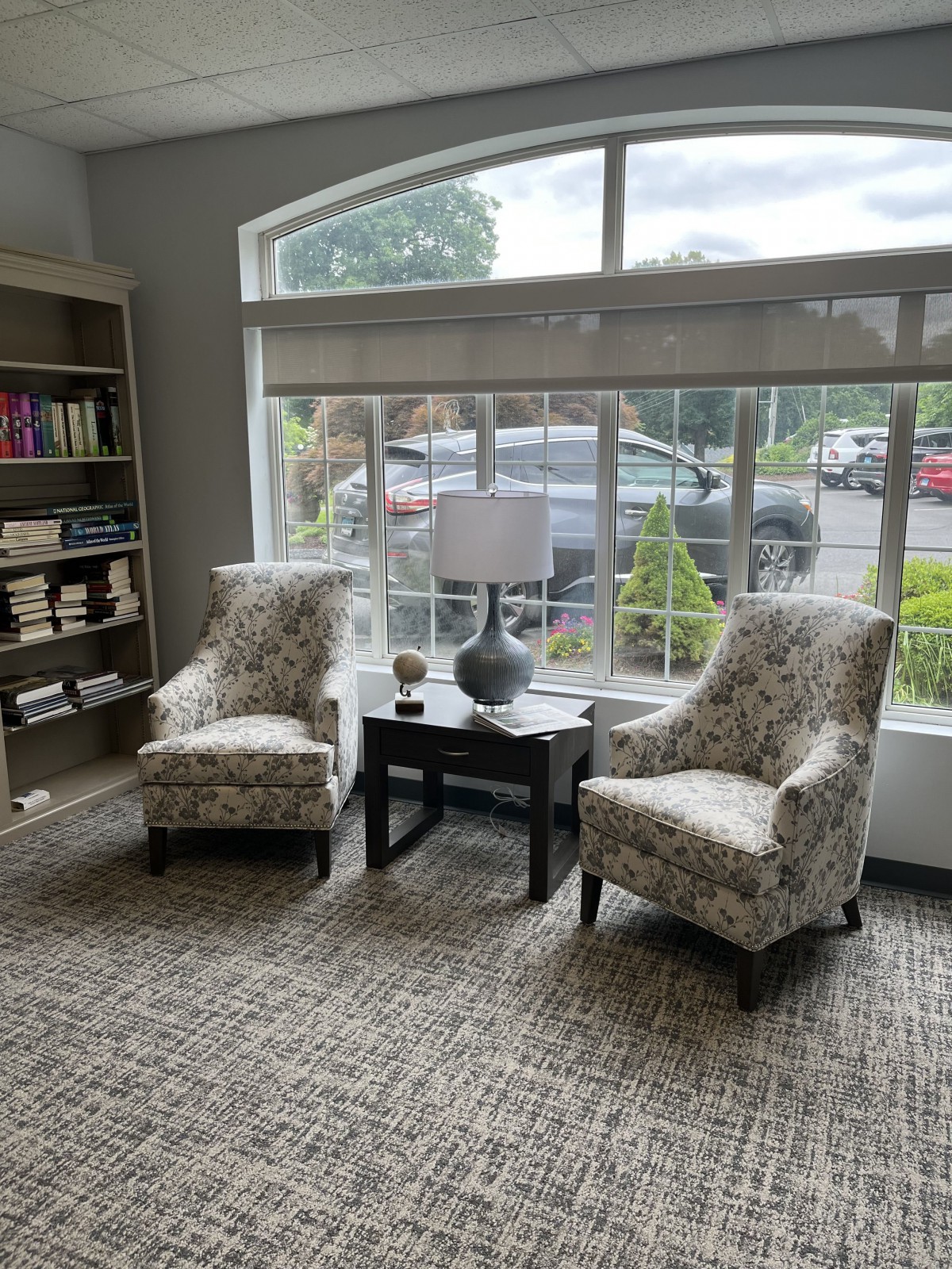 A cozy seating area with two upholstered chairs, a side table with a lamp, and a large window overlooking the outside.