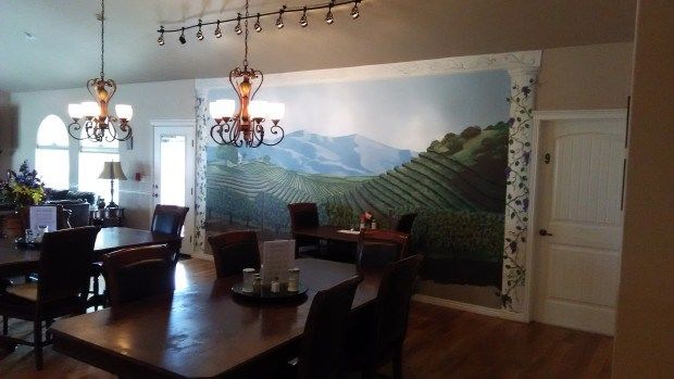 A dining room featuring a large mural of a vineyard landscape and a decorative chandelier.