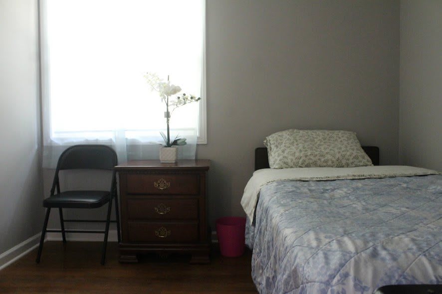 A minimalist bedroom with a single bed, nightstand, and chair by the window.