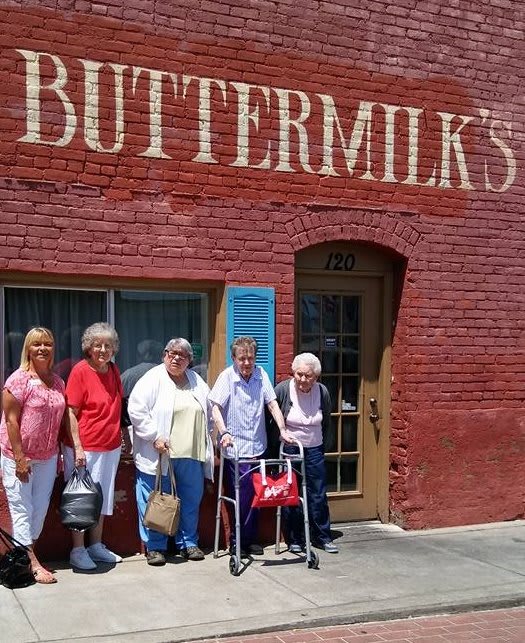 A group of people standing outside a brick building with the sign 'BUTTERMILK'S'.