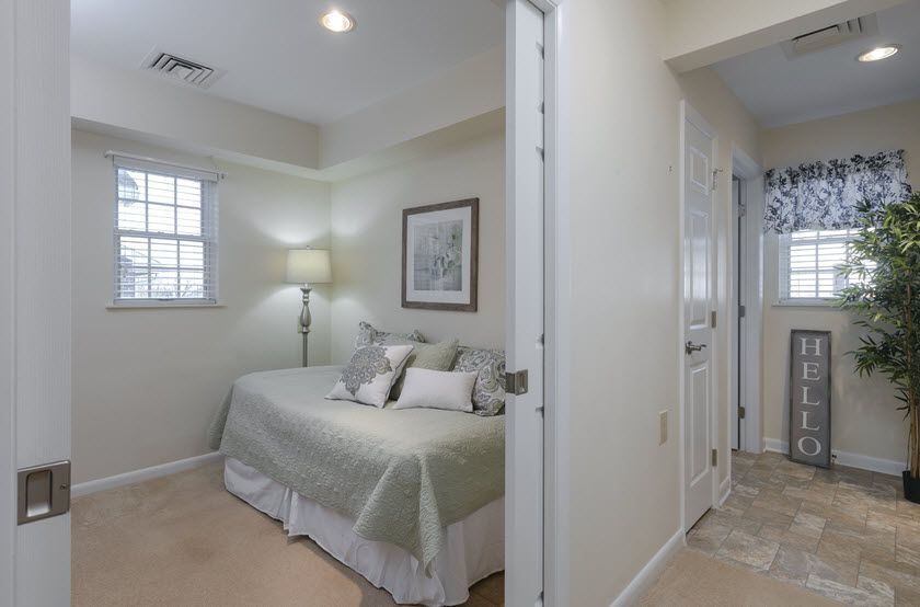 A cozy bedroom with a neatly made bed, soft lighting from a floor lamp, and light-colored decor.