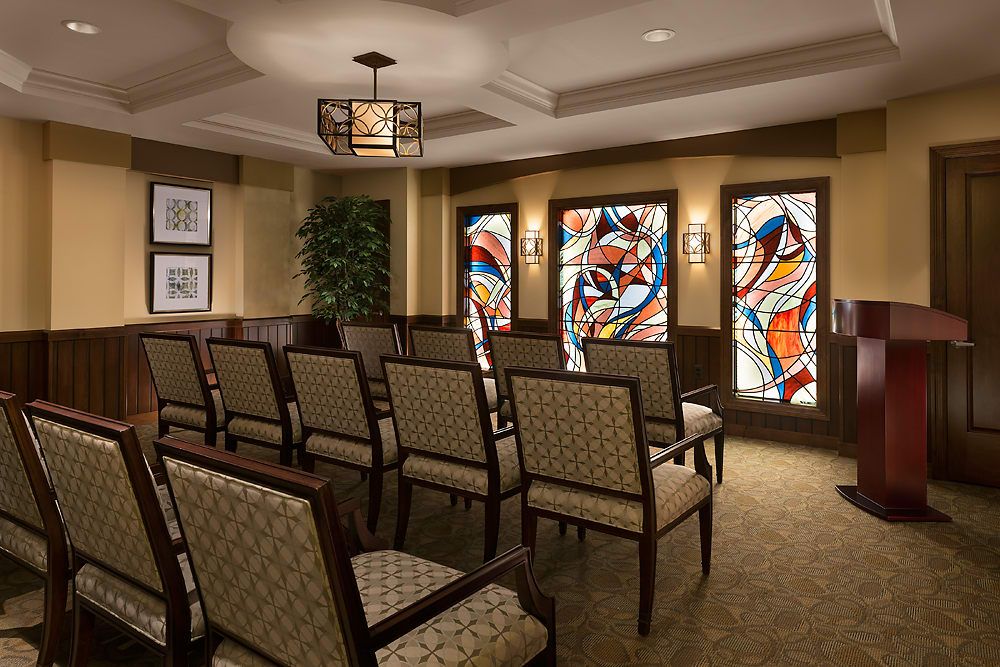 A small chapel with rows of chairs and colorful stained glass windows.