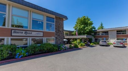 A modern hotel building with stone accents and well-maintained landscaping under a clear blue sky.
