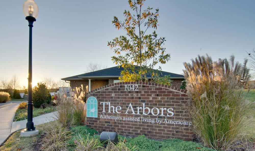 The Arbors assisted living facility sign with a brick base and surrounding greenery.