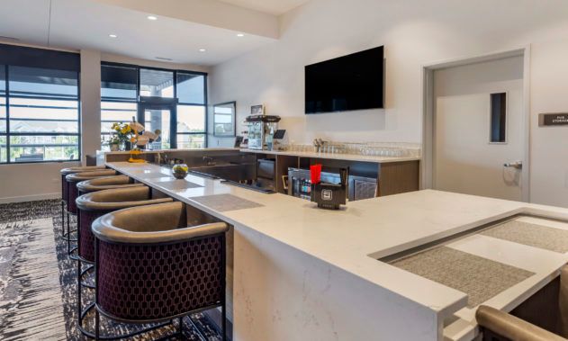 A modern indoor kitchen with a sleek countertop and bar stools, featuring a large television.