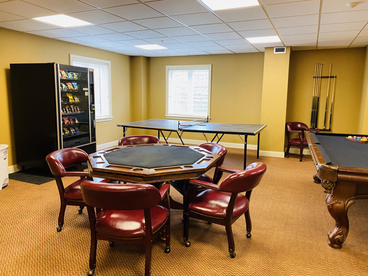 A spacious game room featuring a poker table with red chairs, a vending machine, and a ping pong table.