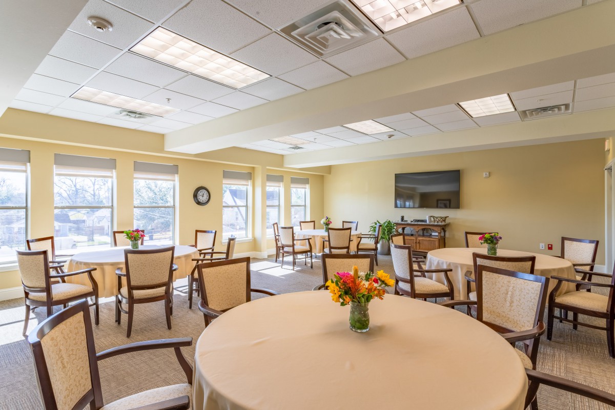 A well-lit indoor dining area with neatly arranged tables and chairs, decorated with flowers.