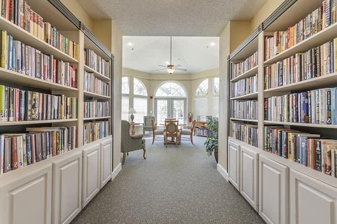 A cozy library with bookshelves lining the hallway, opening up to a well-lit reading area with comfortable seating.