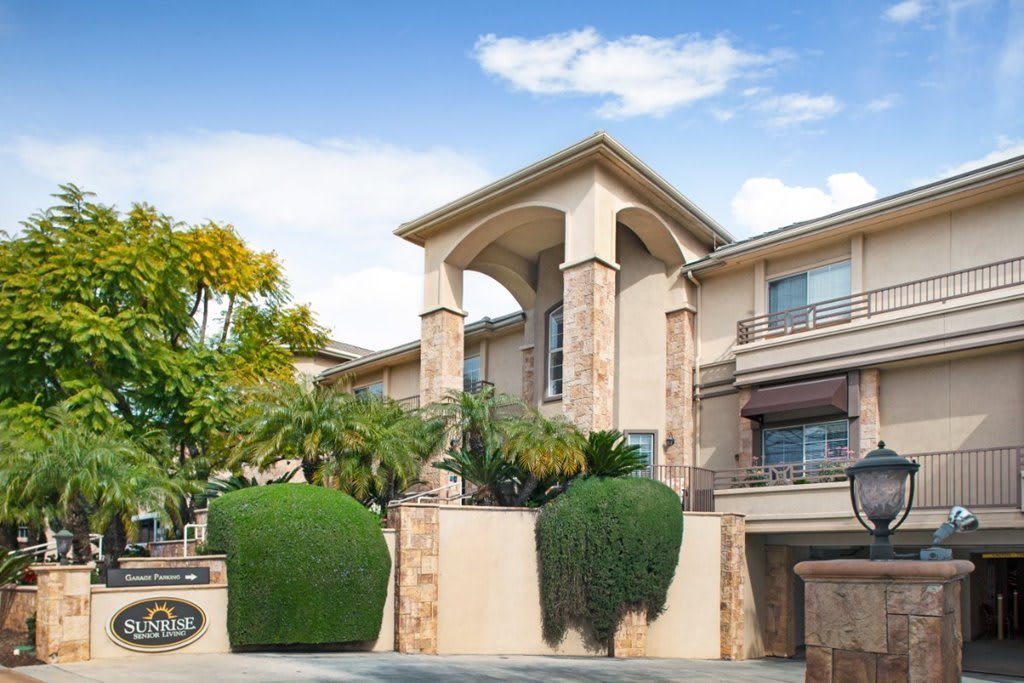A modern, elegant residential building with well-maintained landscaping and a clear blue sky.