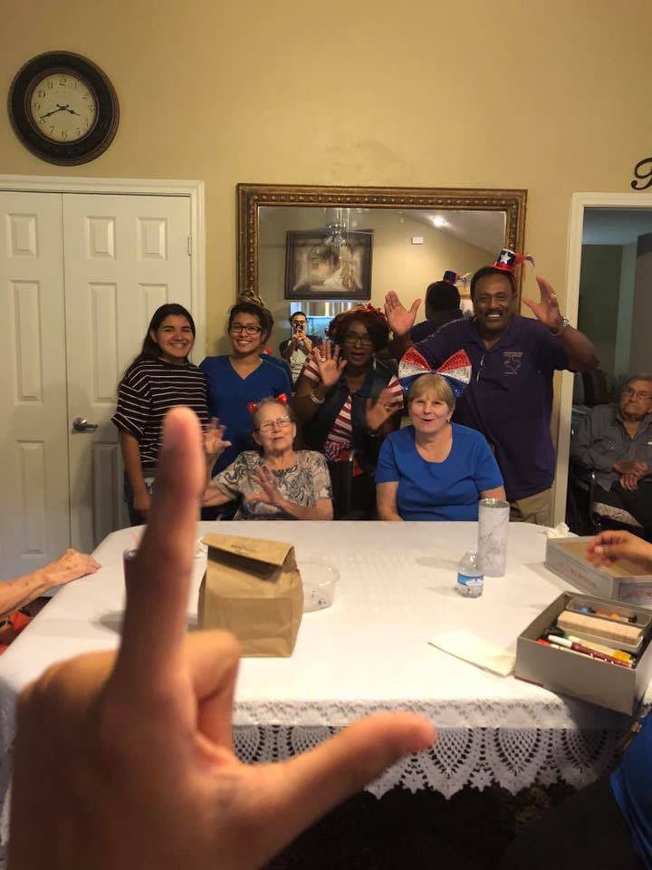 A group of people gathered indoors, wearing party hats and smiling, around a table during a celebration.