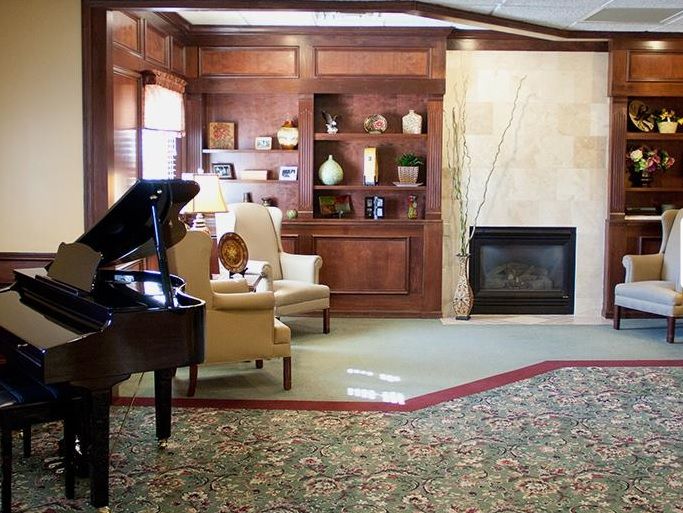 A cozy living room featuring a grand piano, a fireplace, and elegant armchairs.