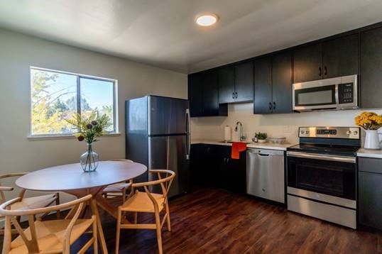 A modern kitchen featuring black cabinets, stainless steel appliances, and a round dining table with chairs.