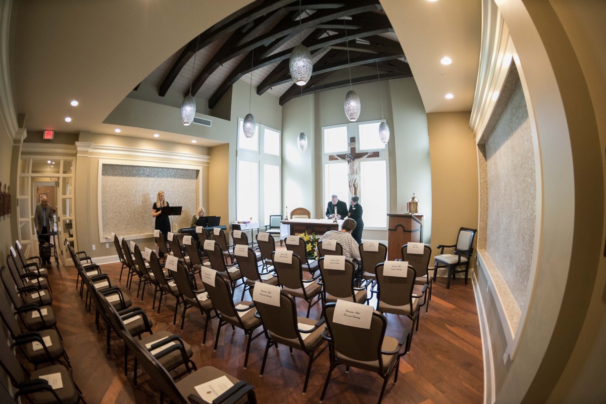 A small chapel with rows of empty chairs facing an altar and a large cross.