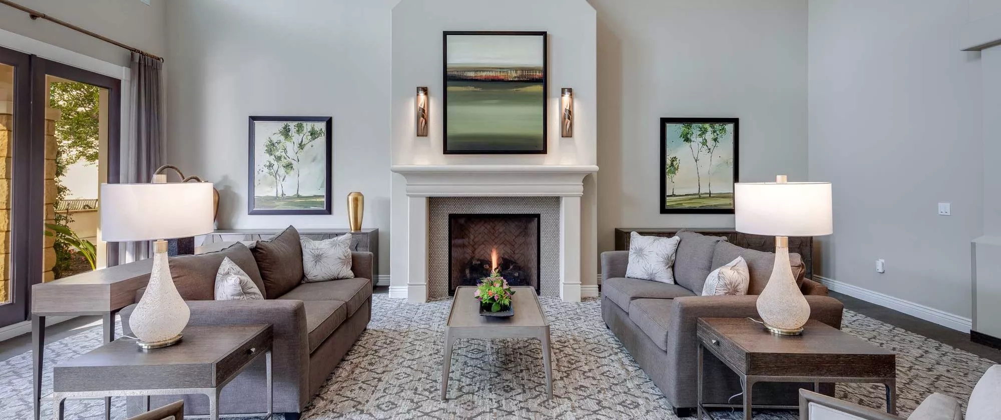 A modern living room features elegant sofas placed symmetrically around a central fireplace, with contemporary artwork adorning the walls.