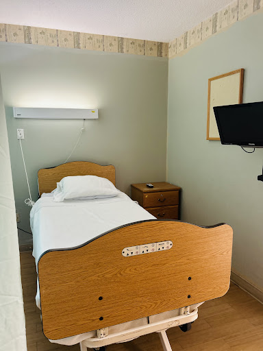 A simple hospital room featuring a single bed, a nightstand, and a wall-mounted TV.