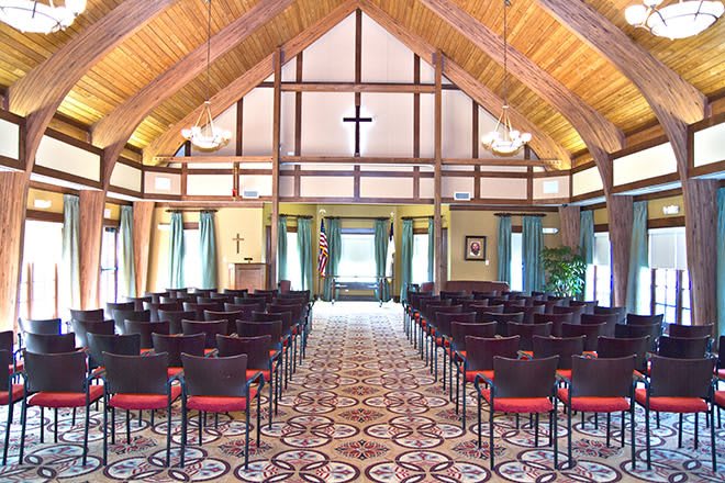 An interior view of a chapel with symmetrical seating and a wooden ceiling.