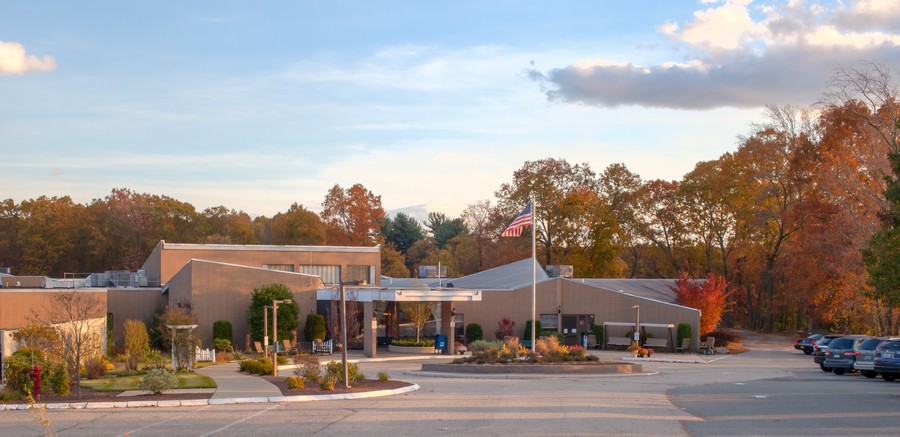 A hospital building with an entrance surrounded by trees under a partly cloudy sky.