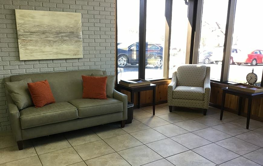 A cozy waiting room with a sofa, armchair, and large windows.