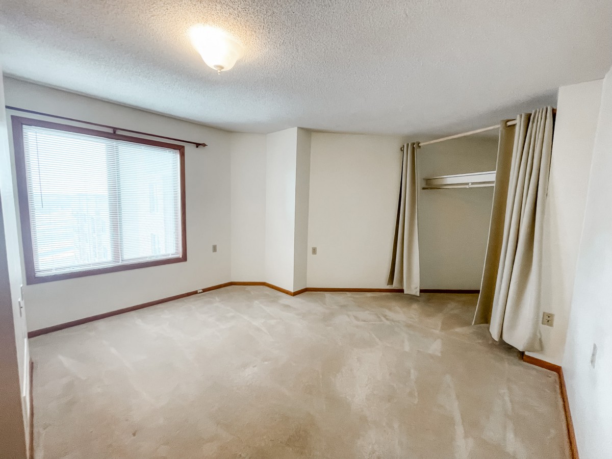 An empty room with a carpeted floor, window, and open closet with curtains.