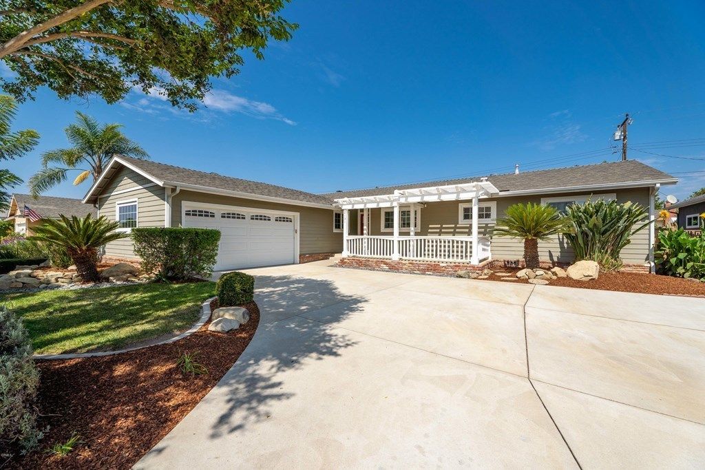 A view of a single-story house with a driveway leading to a garage, surrounded by well-maintained landscaping.