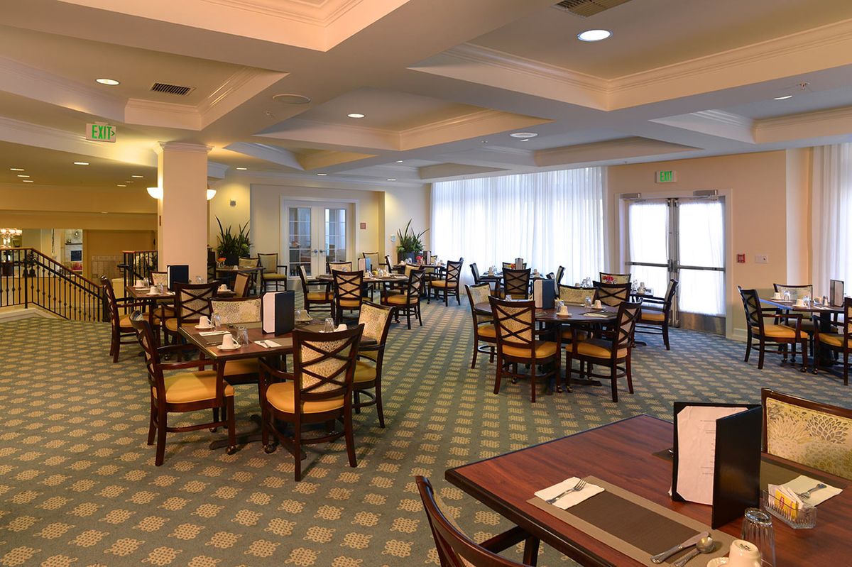 An empty dining room with neatly arranged tables and chairs, featuring a carpeted floor and soft lighting.
