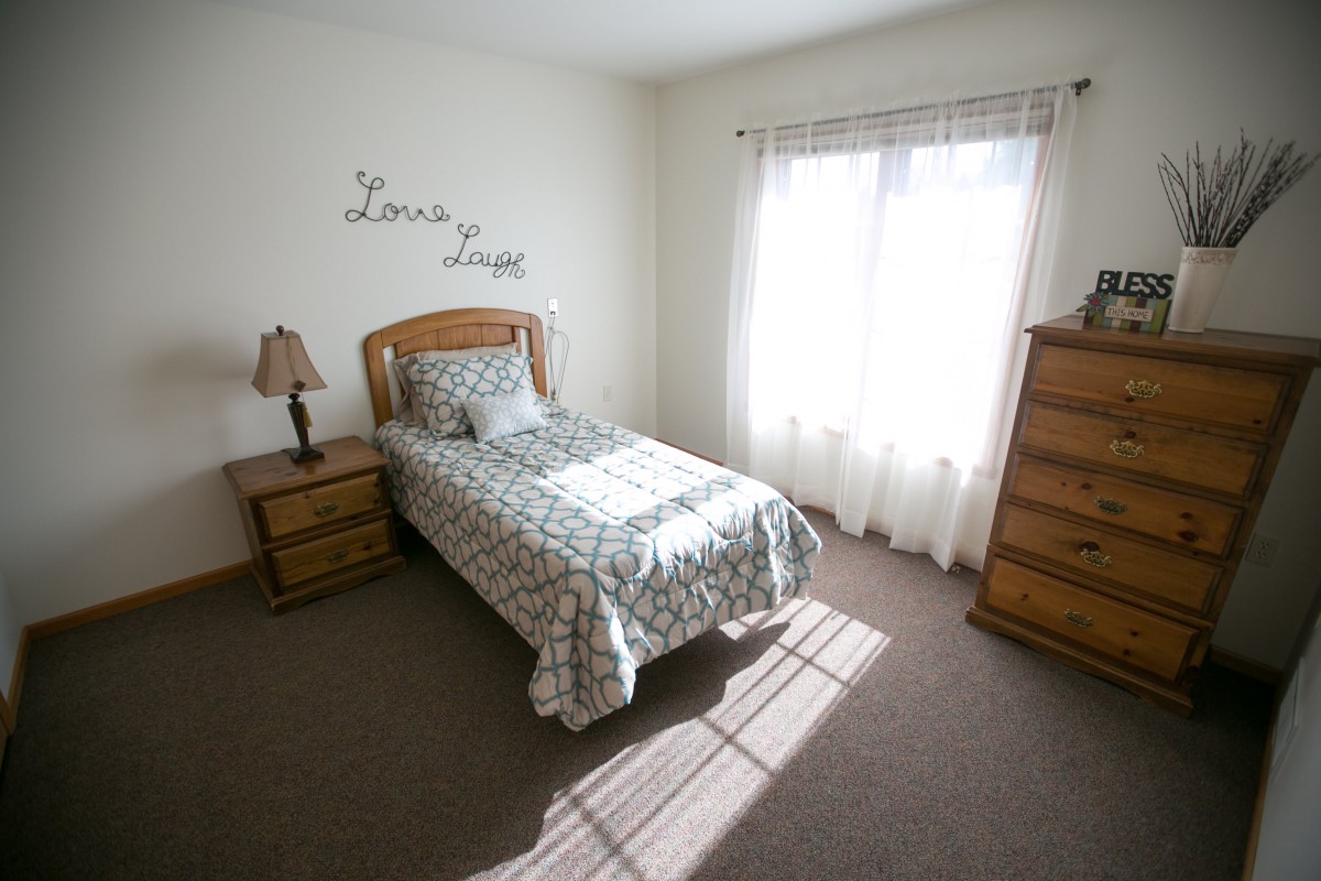 A cozy, minimalist bedroom with a single bed and natural light streaming through the window.
