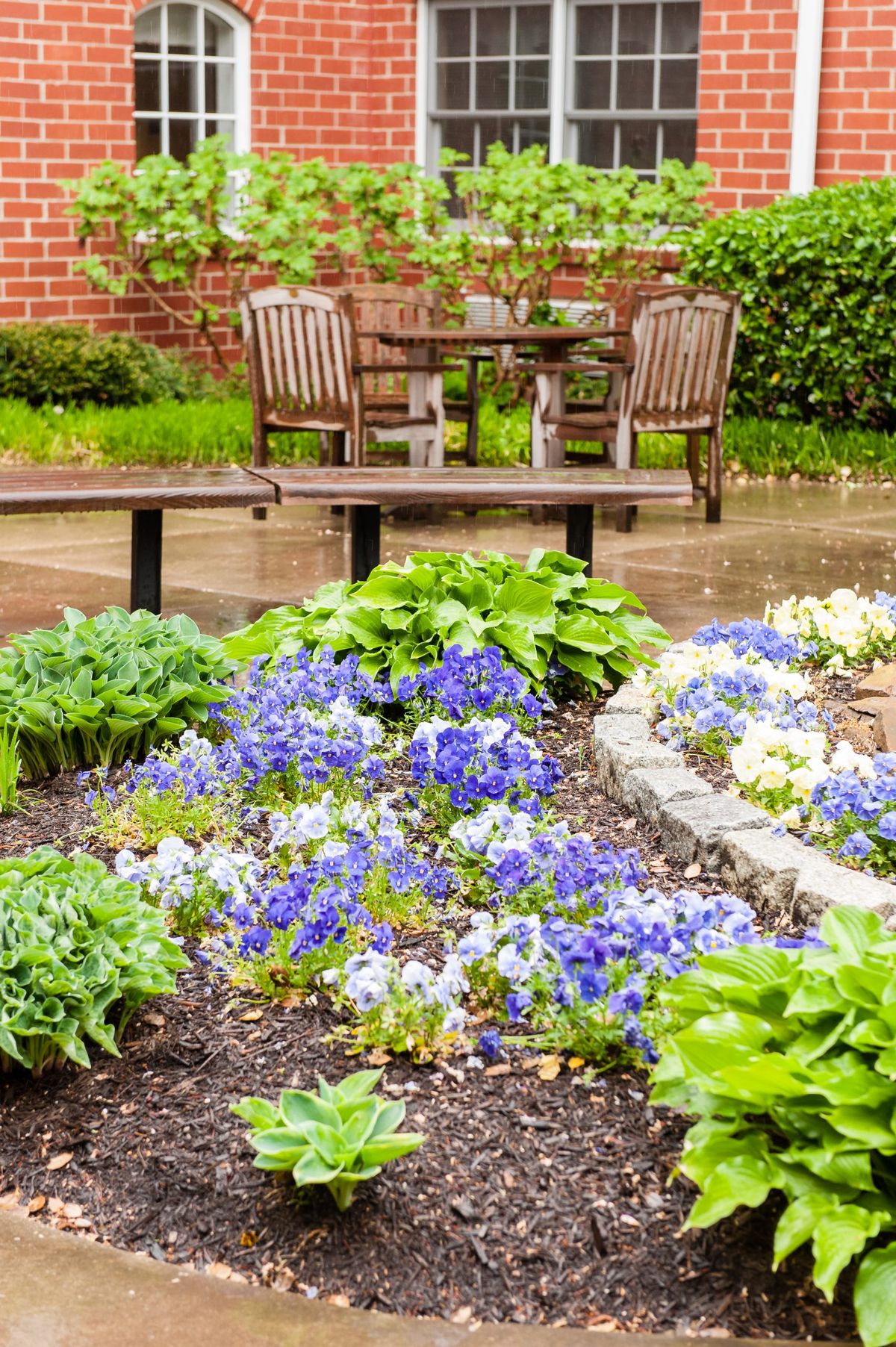 A charming garden scene featuring vibrant flowers and a seating area with wooden furniture.
