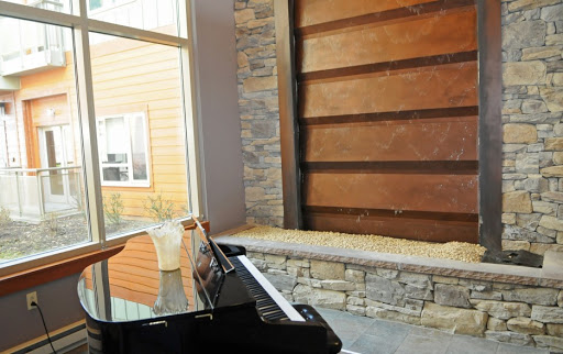 A stylish interior featuring a grand piano beside a stone and wood wall, showcasing modern architectural design.