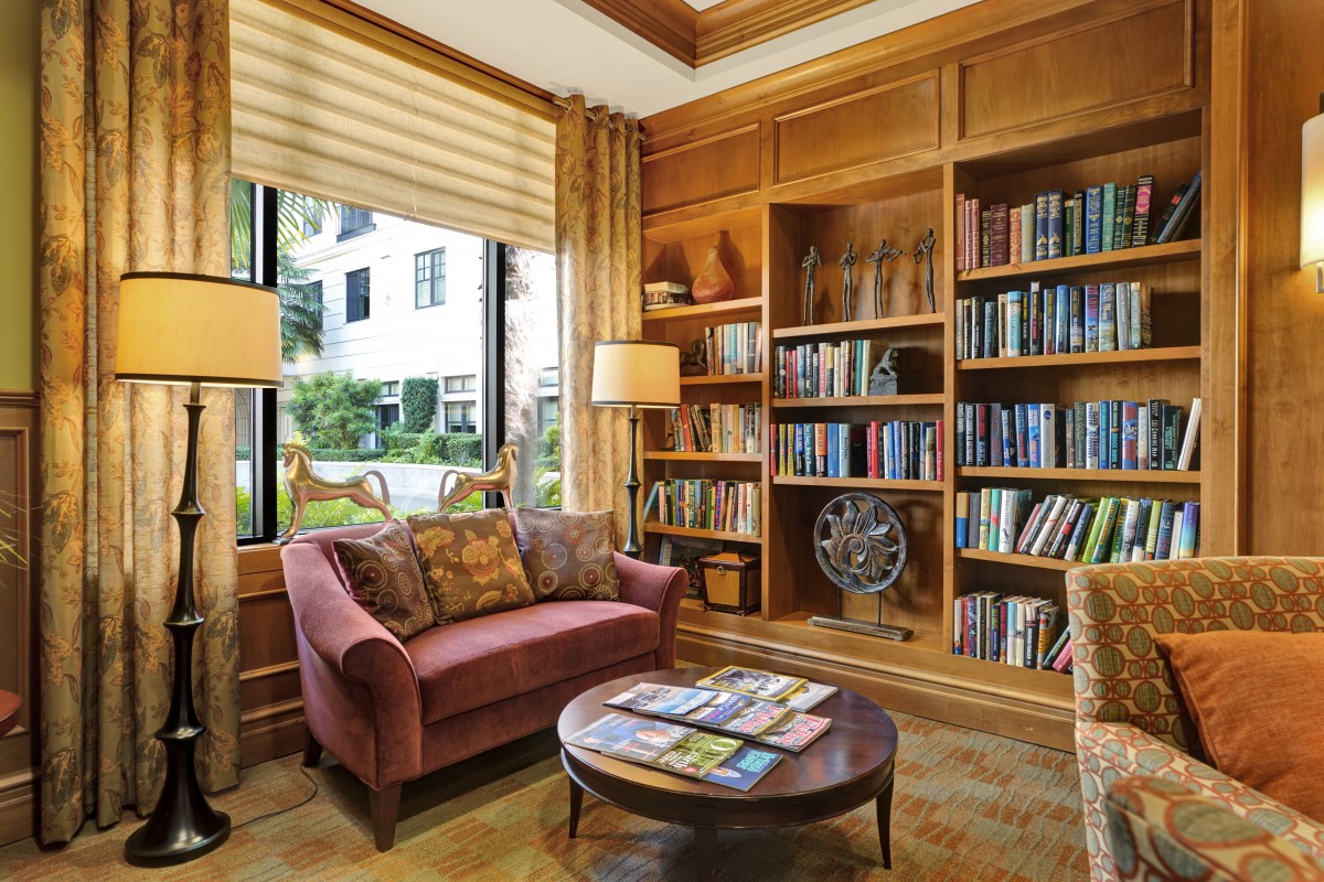 A cozy home library with bookshelves, a sofa, and large windows.