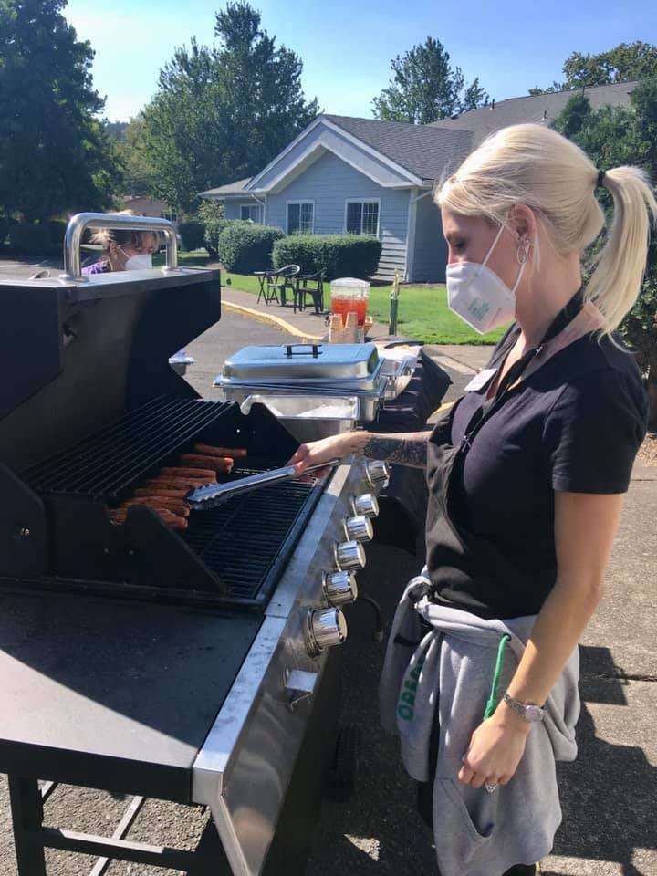 A woman wearing a mask grills food outdoors on a barbecue.