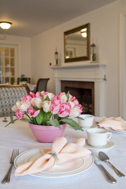 A beautifully set dining table with pink tulips and tea cups in an elegant room featuring a fireplace.