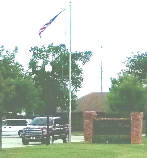A vehicle parked near an entrance with a flag flying at half-mast, surrounded by greenery.