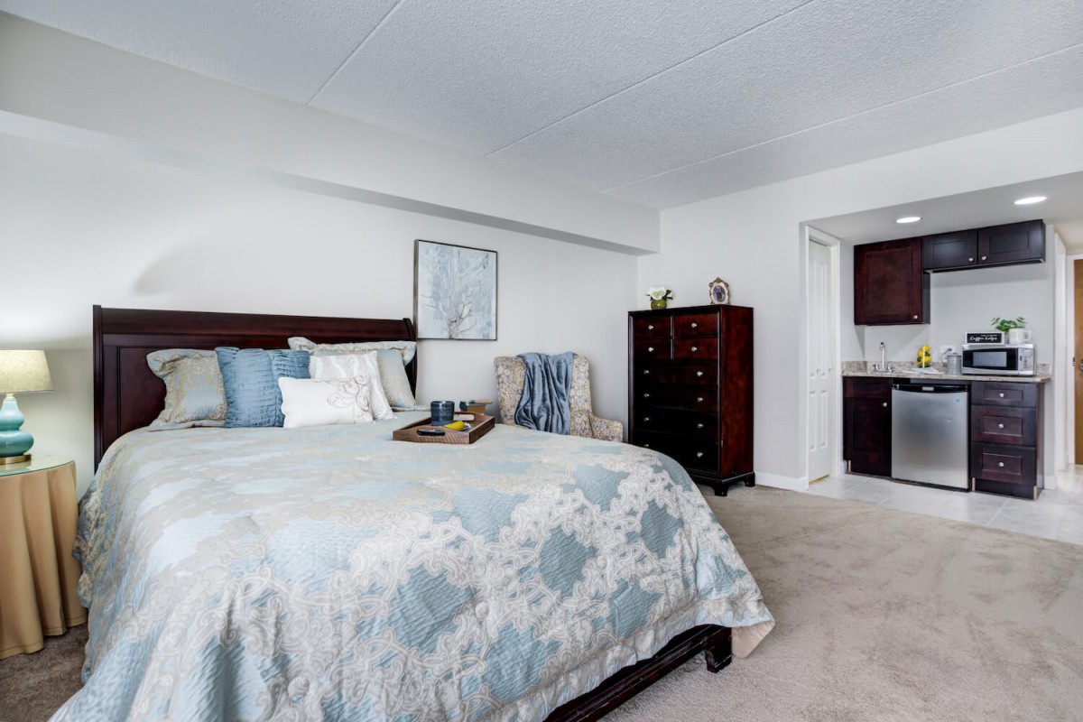 A cozy bedroom featuring a large bed with decorative pillows, a wooden dresser, and soft carpeting.