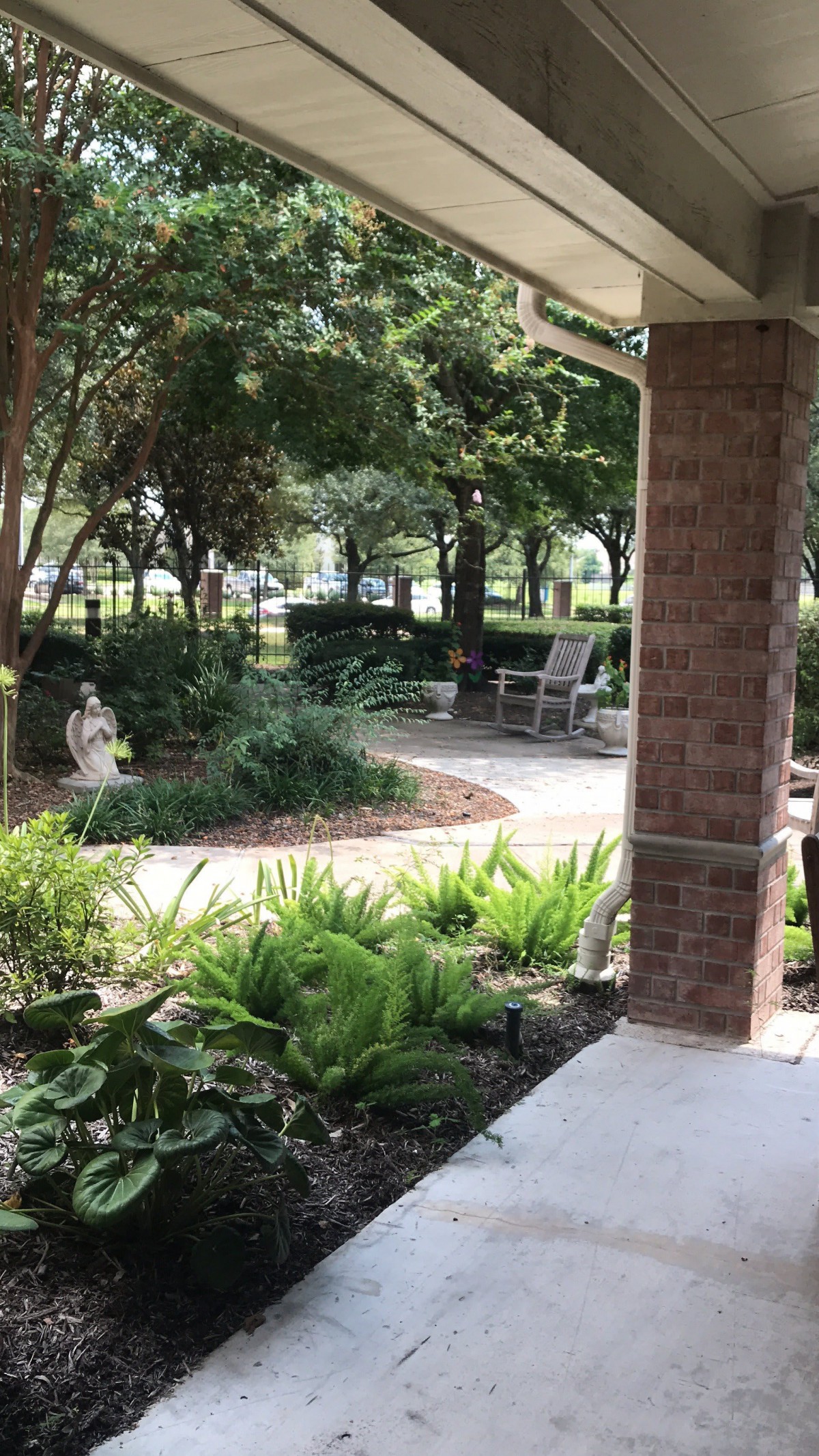 A serene garden with a statue, surrounded by lush greenery and a pathway.
