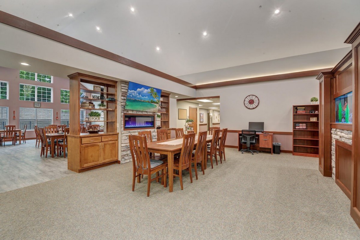 Spacious living area with a dining table, chairs, and a television, complemented by shelves and a computer desk.