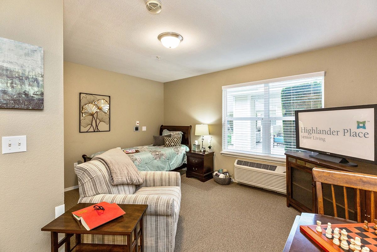 A cozy bedroom with a bed, chair, lamp, and TV by the window.