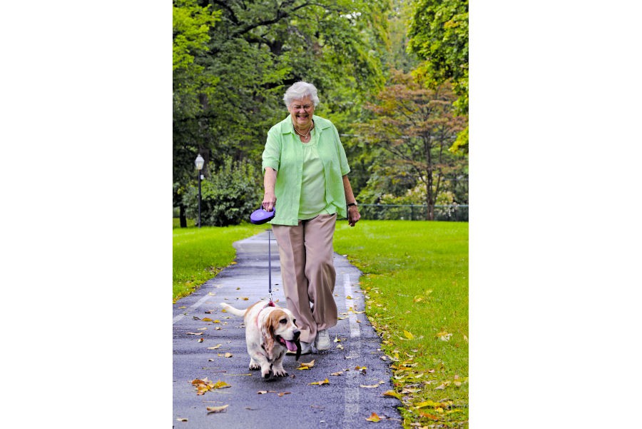An elderly woman taking a leisurely walk with her dog in a park.