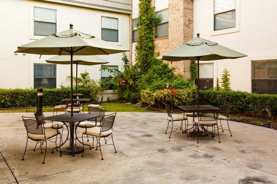 A serene outdoor patio with tables, chairs, and umbrellas surrounded by greenery.