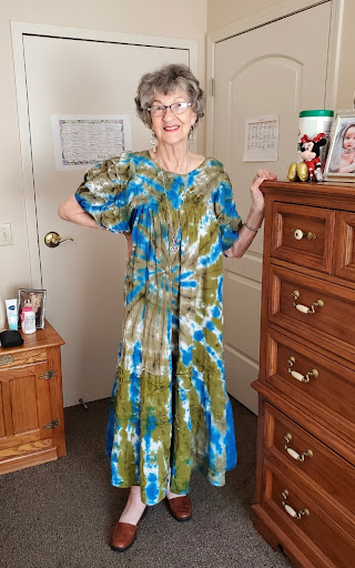 A woman poses in a vibrant tie-dye outfit, showcasing a unique fashion style in her home.