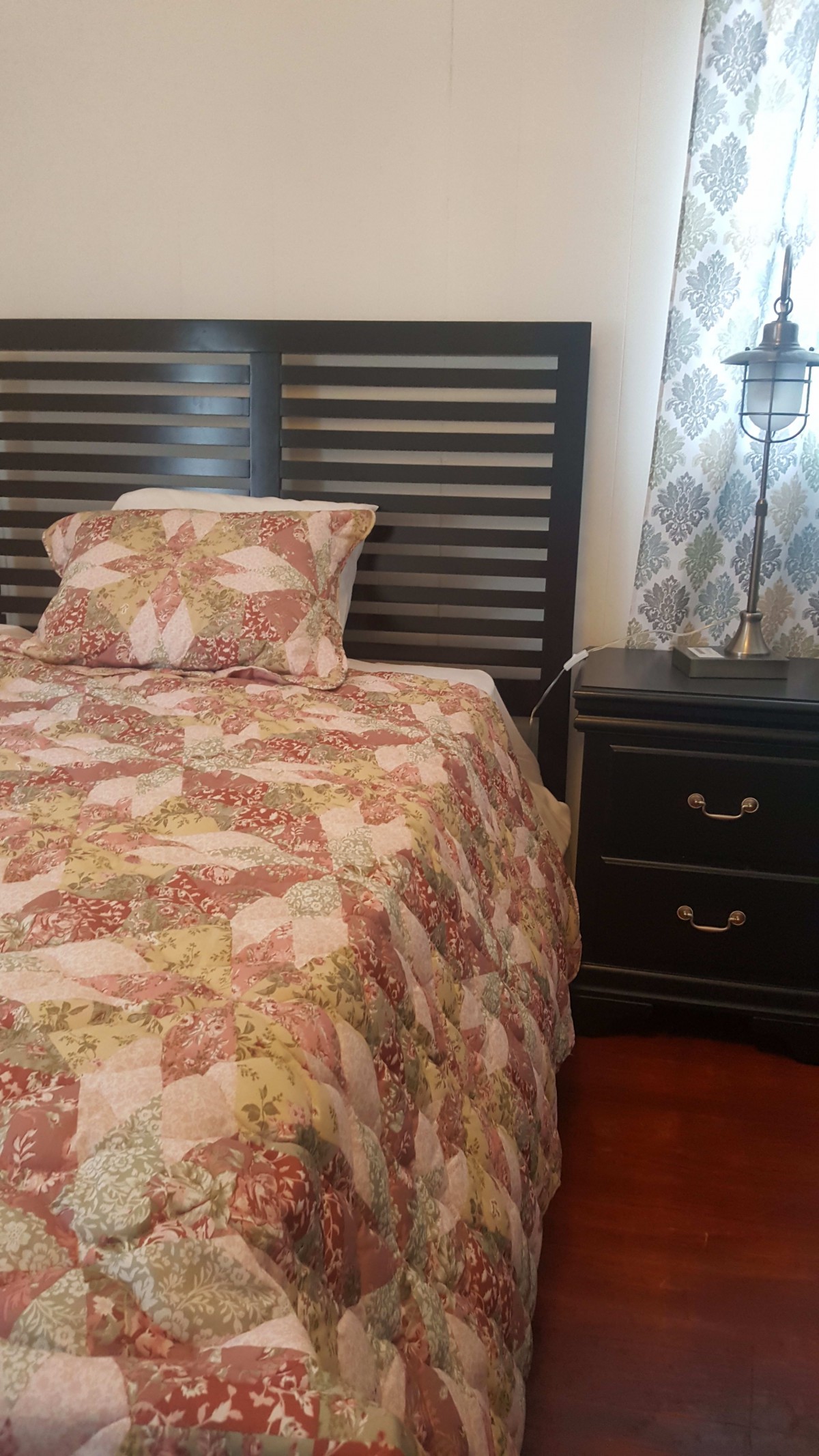 A cozy bedroom with a patterned quilt and matching pillow, featuring a dark wooden headboard and a nightstand with a lamp.