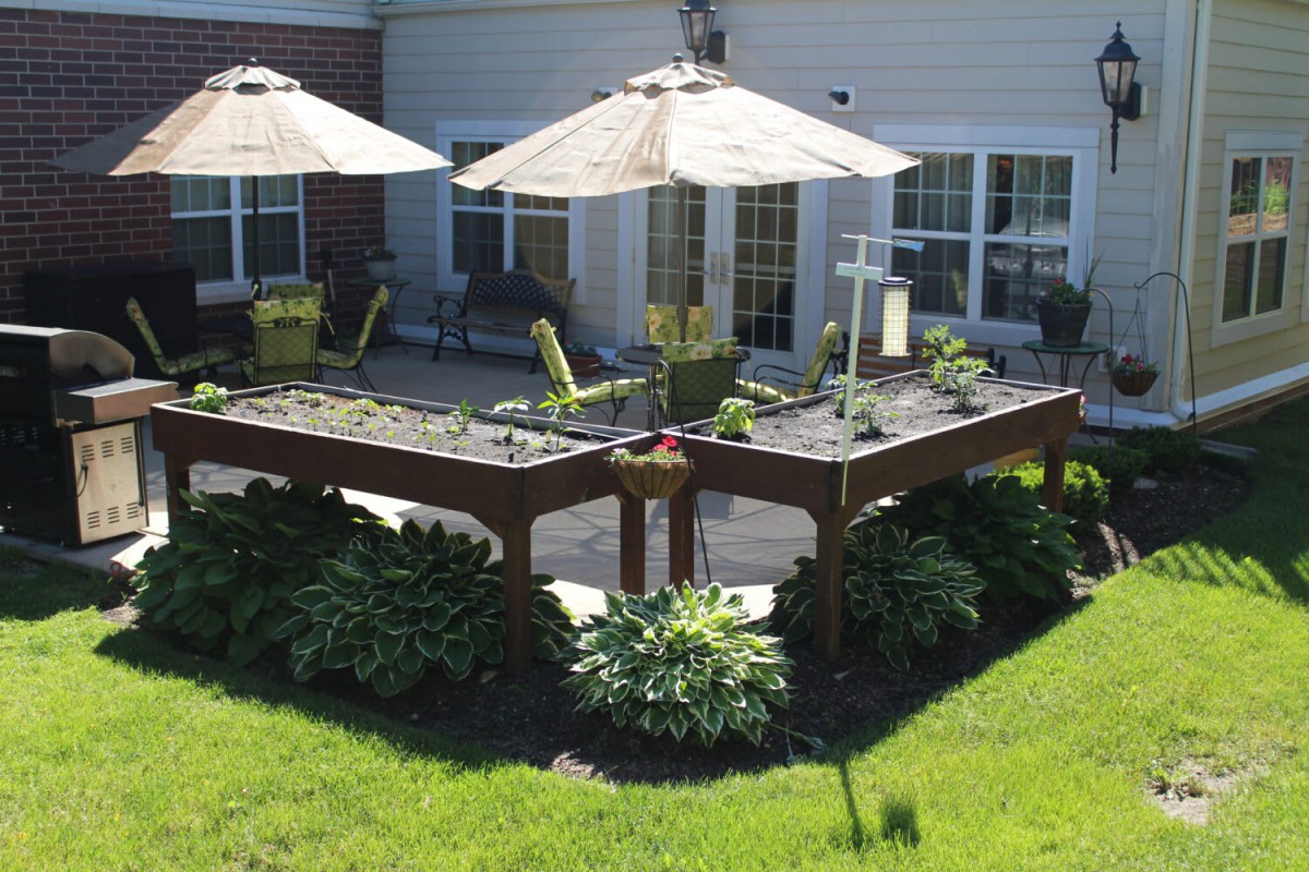 A well-maintained outdoor patio with raised garden beds and seating under large umbrellas.